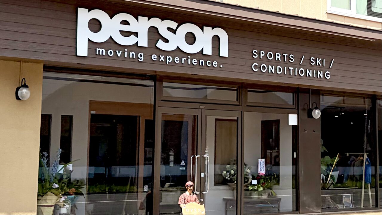 スポーツ専門店PERSON新店舗外観 北海道帯広市東4条南11丁目19番地3 郵便番号080-0804 2026年6月20日土曜日移転リニューアルオープン 元クックチャム帯広店跡地の建物 平屋建て 店舗入口の正面ガラス扉 自動ドア 青い看板 白い文字でPERSON スポーツショップ 十勝のスポーツパートナー ダイイチ東店のすぐ北側 道路沿いの店舗 営業中 駐車場あり NTTの大きな鉄塔から東へ進んだ場所 斉川漢方薬局の隣 帯広駅から車でアクセスしやすい立地 明るい昼間の写真 店舗正面の景色