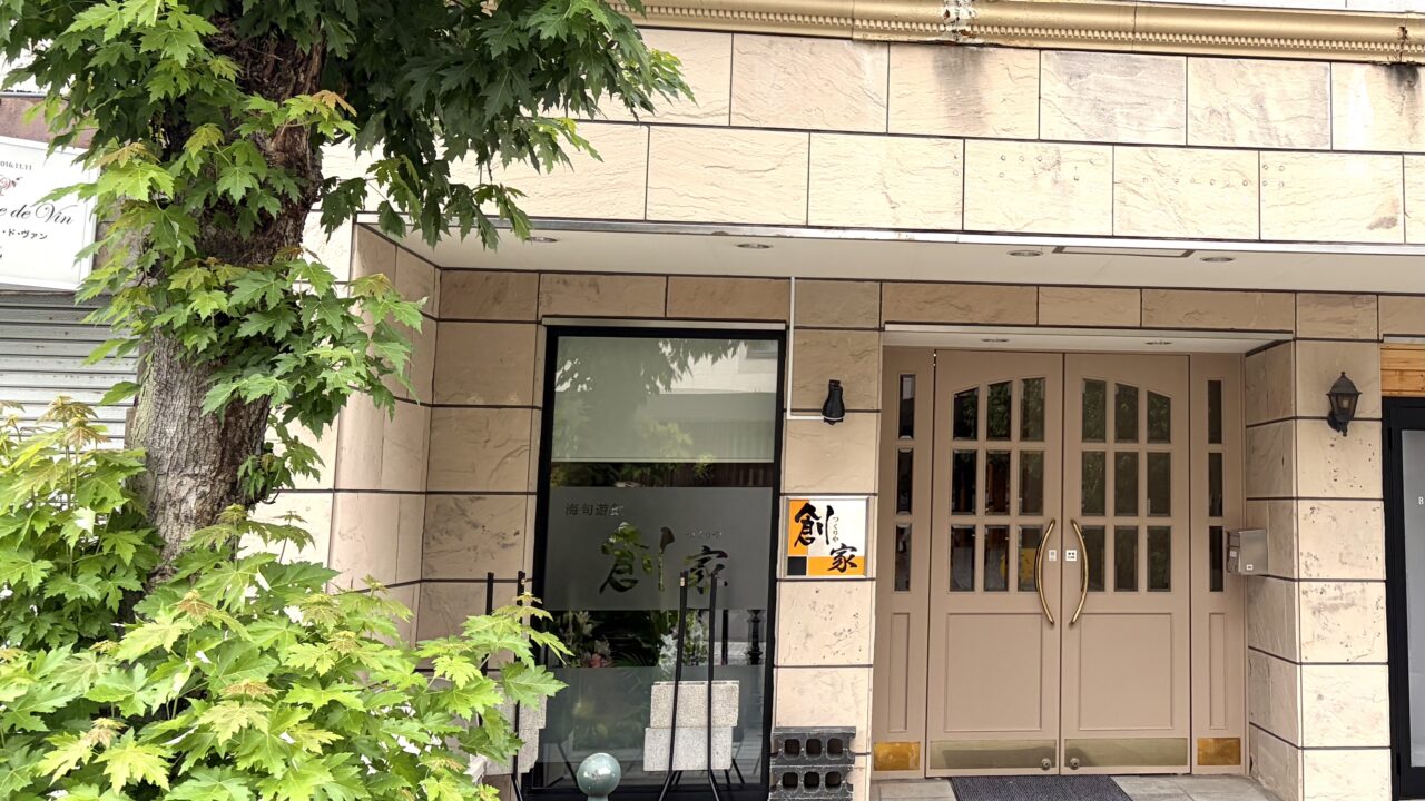 18年間にわたり北の屋台を牽引した名店が卒業し、令和8年(2026年)8月20日(木曜日)に待望の独立グランドオープンを果たした、〒080-0011 北海道帯広市西1条南9丁目3-6の東銀座通り沿いに佇む創作和食店「創家(つくりや)」の真新しい路面店舗の外観全体。地元を代表する銘菓・六花亭帯広本店の駐車場の真向かいという一等地に位置し、新品の香りが漂うような美しく均整の取れた木目の外壁と、モダンで洗練された引き戸のエントランスが美しい平屋風のデザイン。十勝・帯広の新しい美食スポットの誕生を告げる、新しく綺麗な建物が東銀座通りの街並みに調和している様子を捉えた写真。令和8年(2026年)8月20日の新店舗始動に合わせて完全リニューアルされた、〒080-0011 北海道帯広市西1条南9丁目の創作和食店「創家(つくりや)」のファサード(店舗正面)を飾る新しい店舗看板のクローズアップ。これまでの屋台時代の親しみやすさを継承しながらも、より大人の隠れ家としての品格を感じさせるスタイリッシュで美しいフォントで「創家」の文字が立体的に刻まれているデザイン。帯広の夜の繁華街・東銀座通りに集う人々を温かく迎え入れるように、内部からの優しいバックライトが店名を美しく浮かび上がらせており、新時代の幕開けを象徴する、夜の街の新たなランドマークとしての存在感を放っている様子。