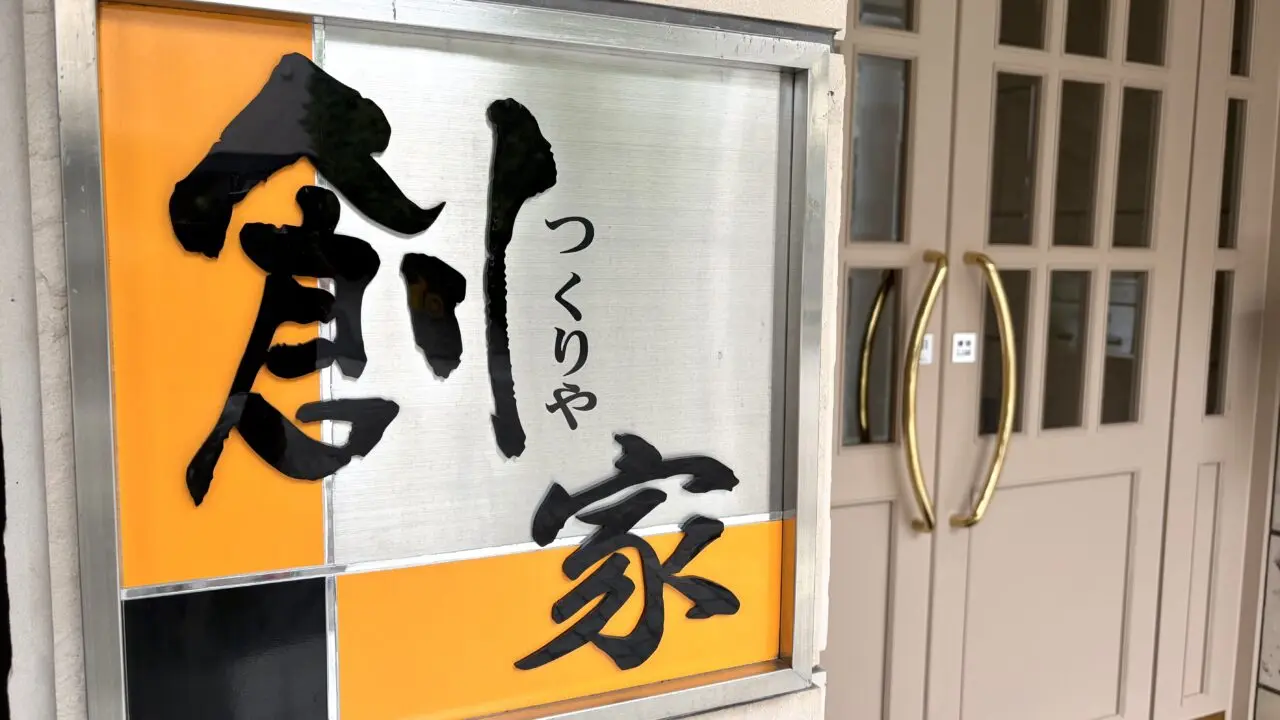 18年間にわたり北の屋台を牽引した名店が卒業し、令和8年(2026年)8月20日(木曜日)に待望の独立グランドオープンを果たした、〒080-0011 北海道帯広市西1条南9丁目3-6の東銀座通り沿いに佇む創作和食店「創家(つくりや)」の真新しい路面店舗の外観全体。地元を代表する銘菓・六花亭帯広本店の駐車場の真向かいという一等地に位置し、新品の香りが漂うような美しく均整の取れた木目の外壁と、モダンで洗練された引き戸のエントランスが美しい平屋風のデザイン。十勝・帯広の新しい美食スポットの誕生を告げる、新しく綺麗な建物が東銀座通りの街並みに調和している様子を捉えた写真。令和8年(2026年)8月20日の新店舗始動に合わせて完全リニューアルされた、〒080-0011 北海道帯広市西1条南9丁目の創作和食店「創家(つくりや)」のファサード(店舗正面)を飾る新しい店舗看板のクローズアップ。これまでの屋台時代の親しみやすさを継承しながらも、より大人の隠れ家としての品格を感じさせるスタイリッシュで美しいフォントで「創家」の文字が立体的に刻まれているデザイン。帯広の夜の繁華街・東銀座通りに集う人々を温かく迎え入れるように、内部からの優しいバックライトが店名を美しく浮かび上がらせており、新時代の幕開けを象徴する、夜の街の新たなランドマークとしての存在感を放っている様子。